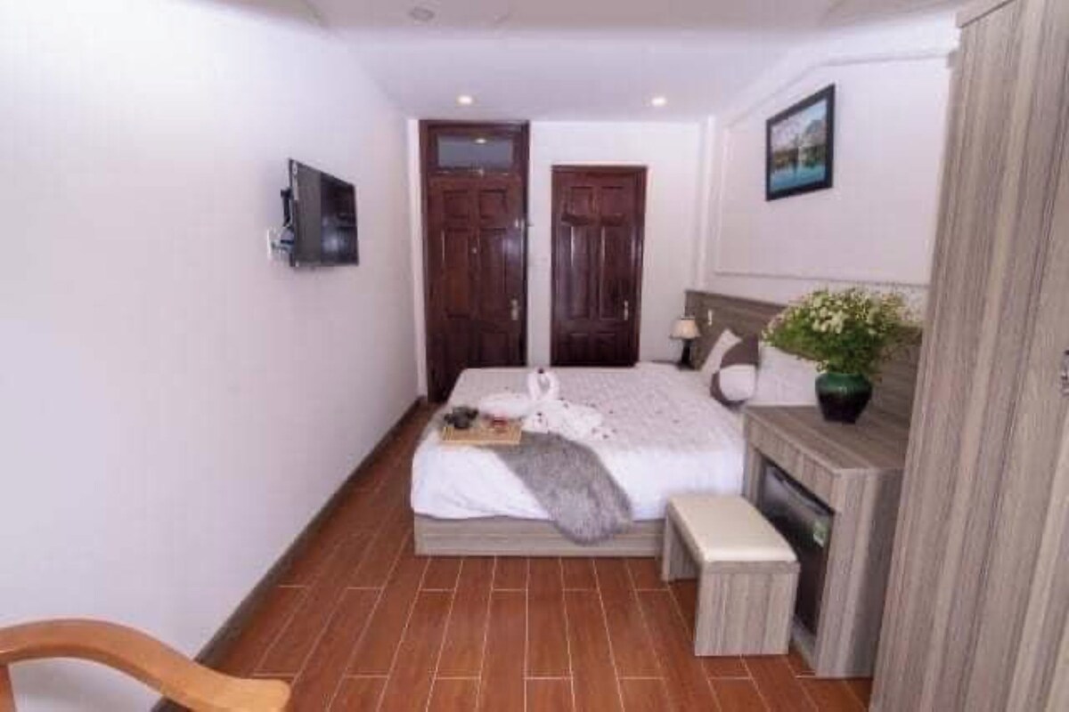 Un dormitorio con cama, mesita de noche, una silla, chimenea y televisor montado en la pared.