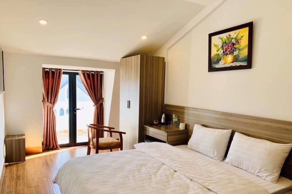 A hotel room with a large bed, a chair, a nightstand, and a painting on the wall.