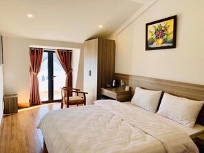 A hotel room with a large bed, a chair, a nightstand, and a painting on the wall. - Lina Hotel (Lam Vien - Da Lat)