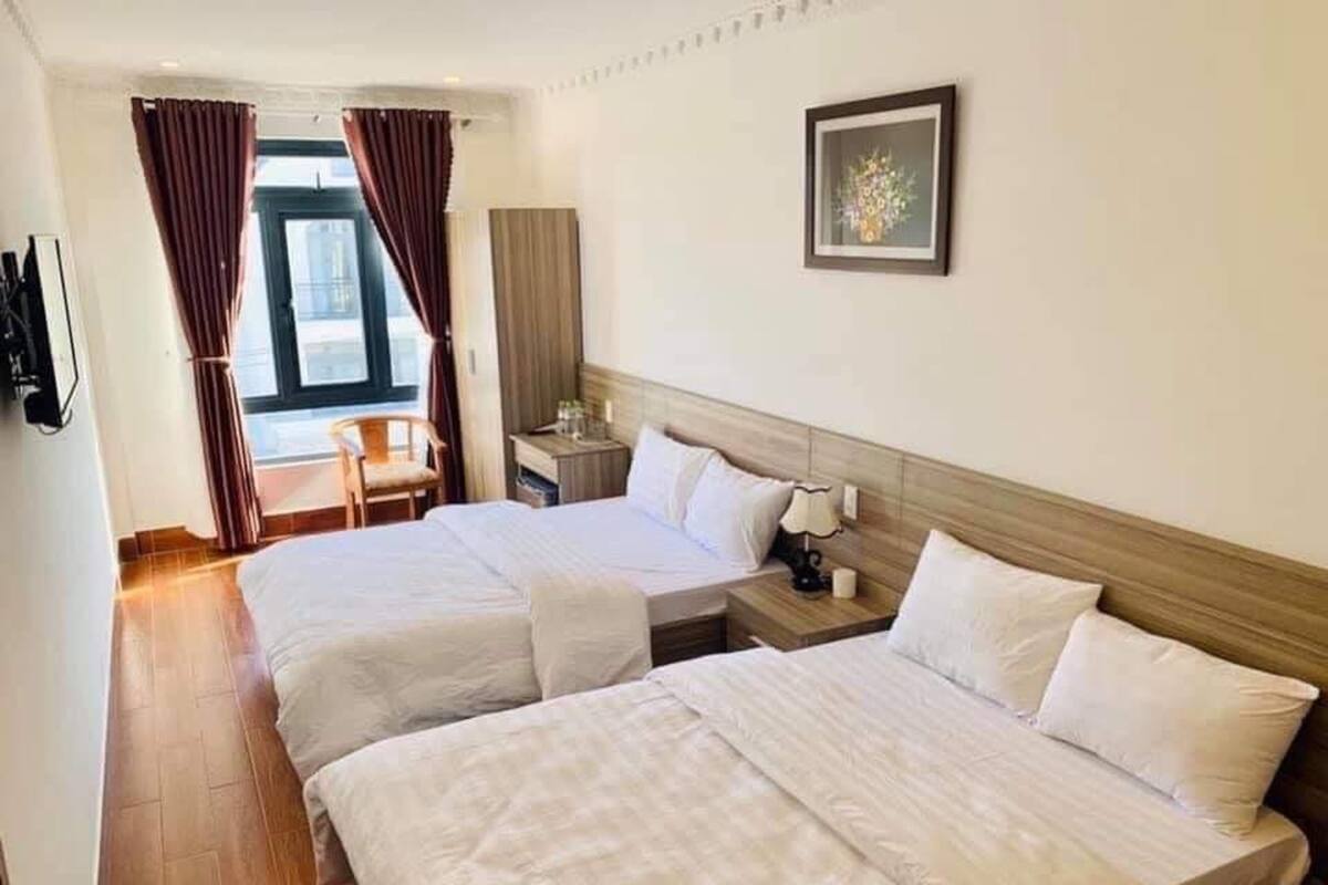 A hotel room with two beds, a desk, a chair, a nightstand, and a window with curtains.