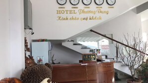Zona de recepción de un hotel con relojes mostrando diferentes husos horarios, un mostrador de recepción y una escalera que conduce a un piso superior.