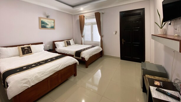 Habitación de hotel con dos camas, un televisor de pantalla plana, un escritorio con control remoto y una ventana con cortinas.