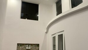 Una habitación con techo curvo, iluminación empotrada, ventana con vistas y termostato en la pared.