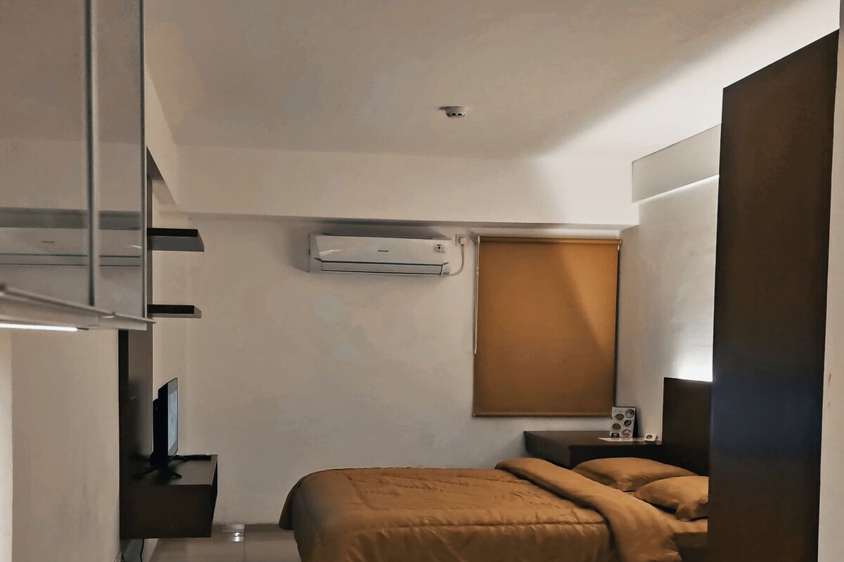 Una habitación de hotel moderna con cama, mesita de noche y un pequeño escritorio con silla.