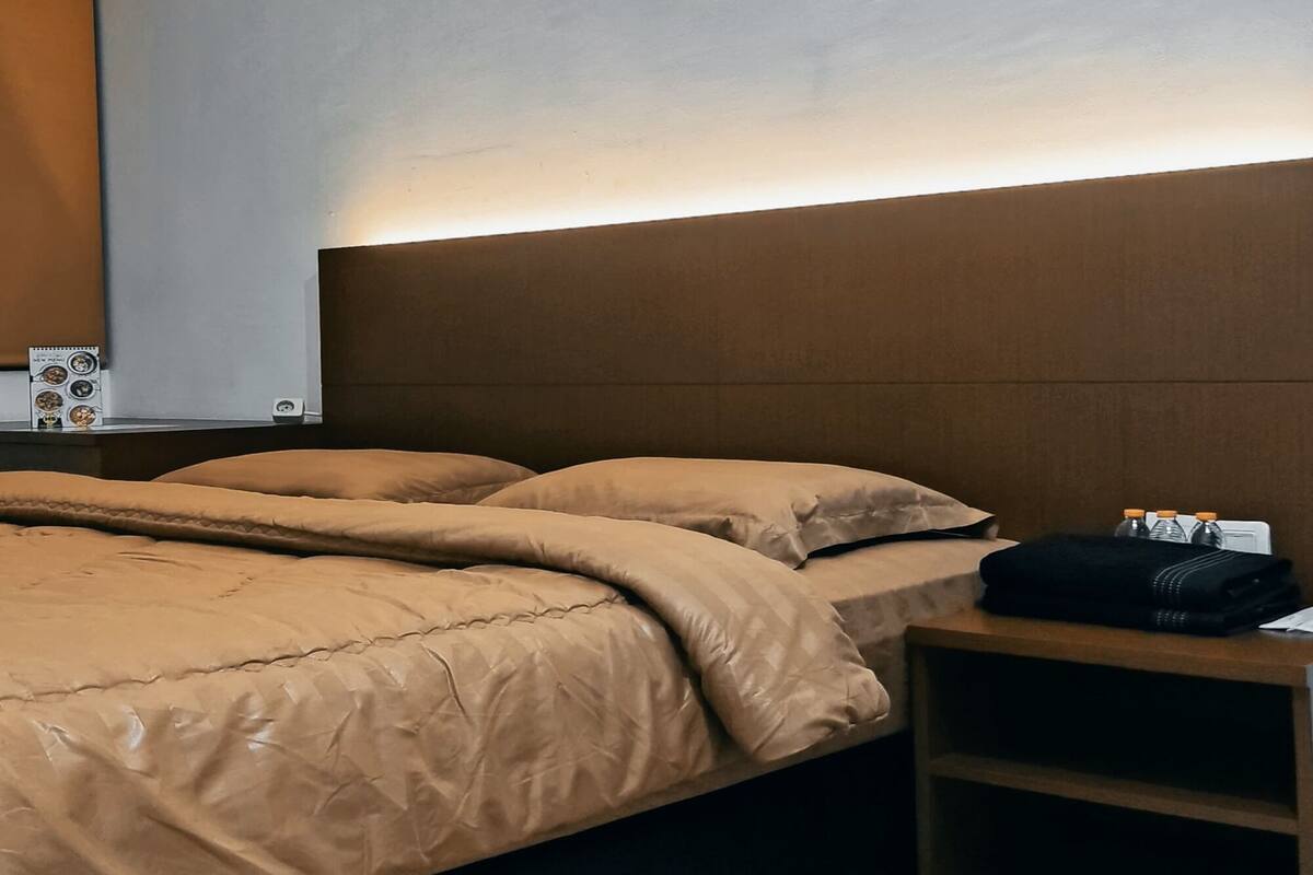 A modern hotel room with a large bed, a nightstand, and a wall-mounted light.
