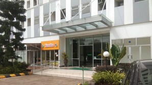 A modern building with a glass entrance, a sign for 'Yamiku', and a parking area with yellow and black curbs. - Dinda Apartment Gunung Putri Square (Gunung Putri)