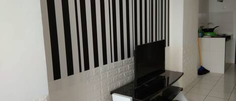 A modern living room with a black TV stand, a white textured wall, and a kitchen area in the background.