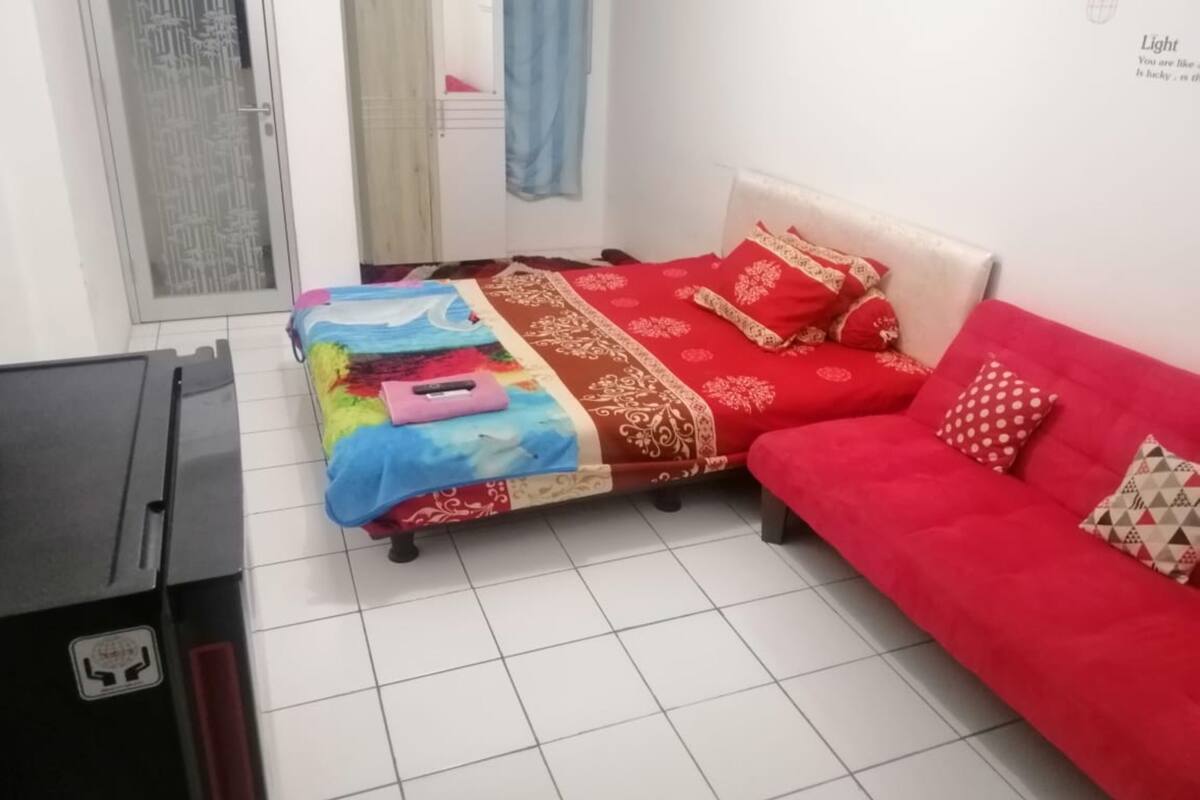 A bedroom with a bed, a red sofa, a desk, and a window with curtains.