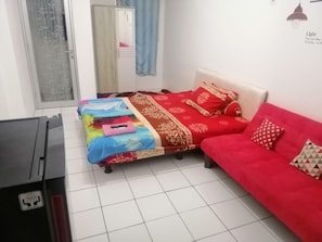 Un dormitori amb un llit, un sofà vermell, un escriptori i una finestra amb cortines.