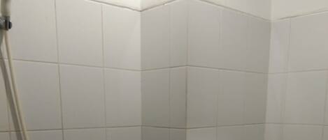 A bathroom with white tiles, a shower, a toilet with a humorous inscription, and a black trash bin.