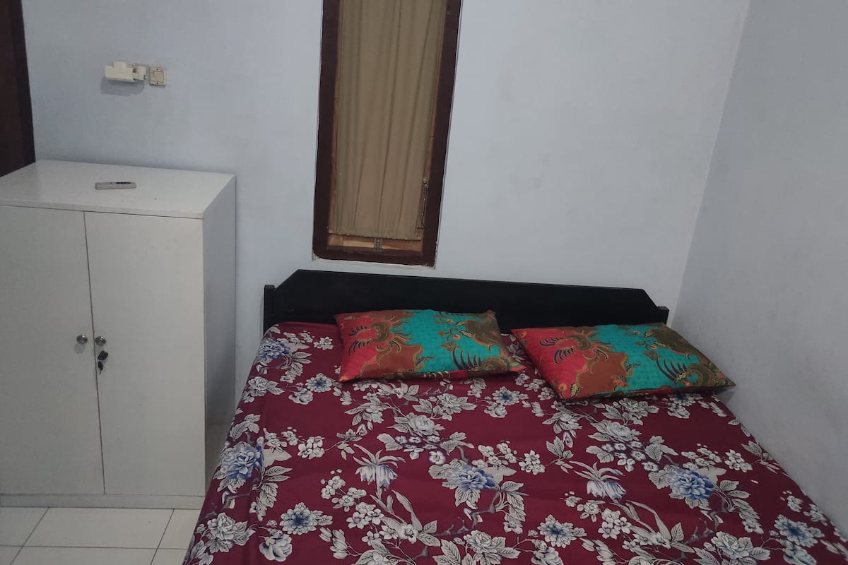 A small room with a bed, a wardrobe, and a window with curtains.