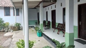 Un espacio al aire libre techado con una banca, plantas en macetas y un edificio con tejado de tejas.
