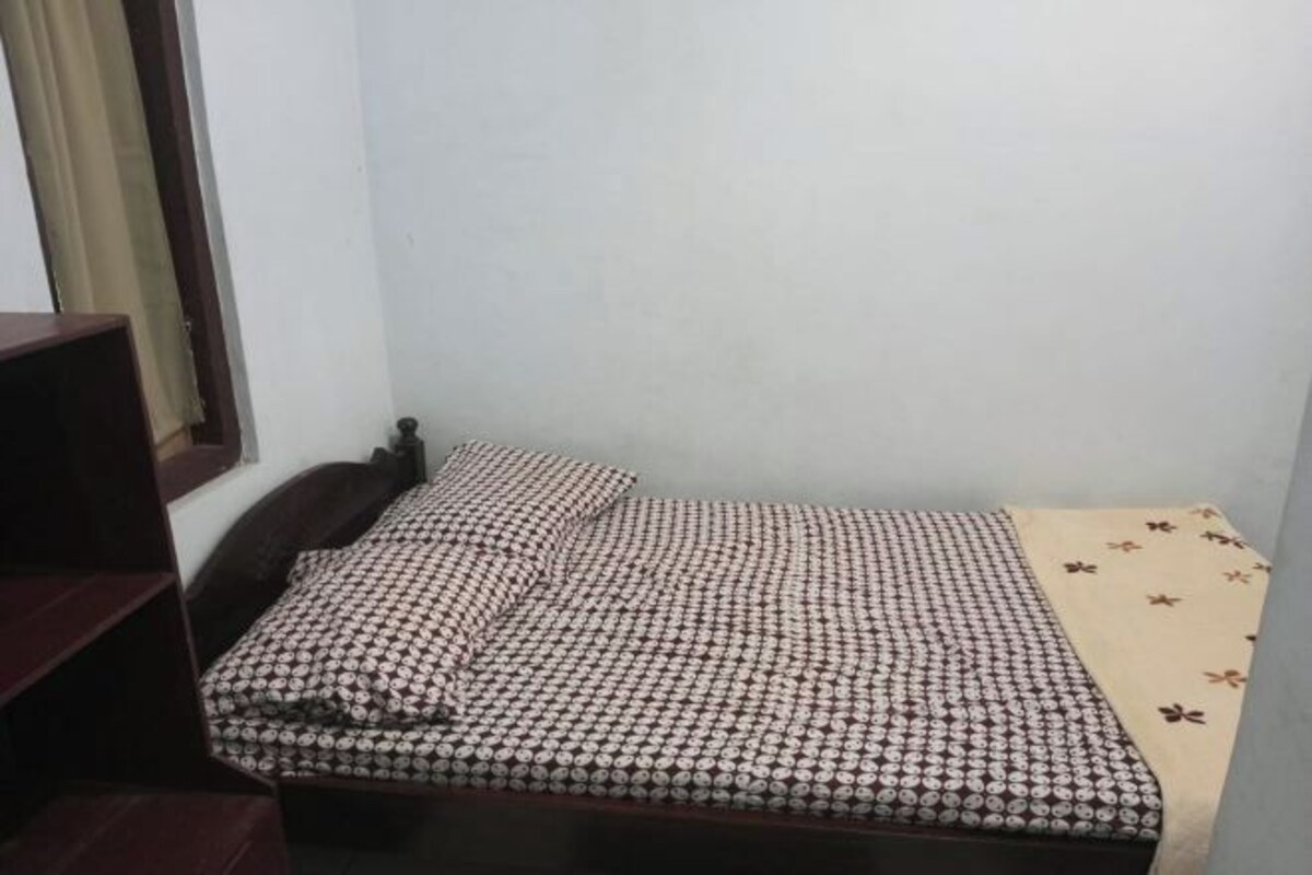 Una habitación pequeña con cama individual, una colcha estampada y una manta color beige.