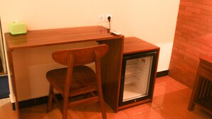 Una habitación compacta con un escritorio de madera, una silla y un refrigerador pequeño.