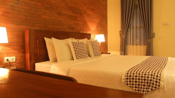Habitación de hotel con pared de ladrillo, cabecera de madera, y cama con almohadas estampadas y manta a rayas.