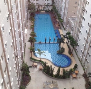 Un edificio de gran altura con una piscina central rodeada de palmeras y sillas de descanso.