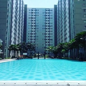 A swimming pool surrounded by tall residential buildings with a clear sky above. - Apartement Puncak Kertajaya New By Prafi (Surabaya)