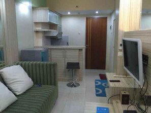 Un espacio habitable pequeño y funcional con sofá, una mesita, televisor y una zona de kitchenette.