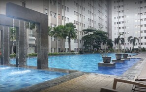 Una piscina con caída de agua, rodeada por un edificio de gran altura con varios balcones.