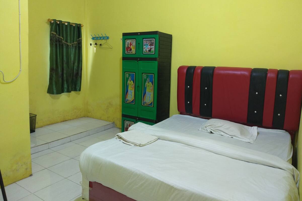 A room with a bed, a green cabinet with pictures, a curtain, and a tiled floor.