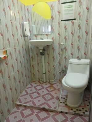 Ein Badezimmer mit Toilette, Waschbecken und Dusche. Die Wände sind mit einem Blumenmuster versehen, und der Boden hat ein geometrisches Fliesenmuster.