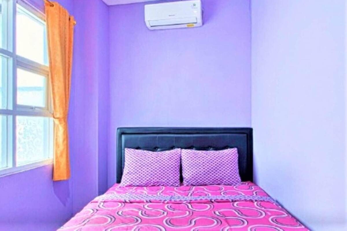 A room with a bed, a window with curtains, and an air conditioning unit on the wall.
