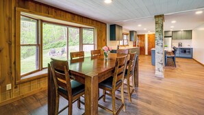 Un comedor con una mesa y sillas de madera, ventanas amplias y vistas al exterior.