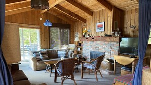 A cozy cabin interior with a wooden ceiling, a fireplace, a sofa, a dining table, and a television. - WestWind Georgian Bay Muskoka Cottage Retreat Private Access (Sleeps Max 8) (MacTier)