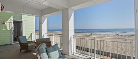A covered outdoor area with a view of the beach, furnished with wicker chairs and a wooden table.