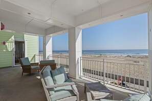 Een overdekt terras met uitzicht op het strand, ingericht met rieten stoelen en een houten tafel.
