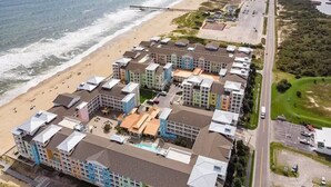Una vista aerea di un hotel sulla spiaggia con diversi edifici, una spiaggia e un molo.