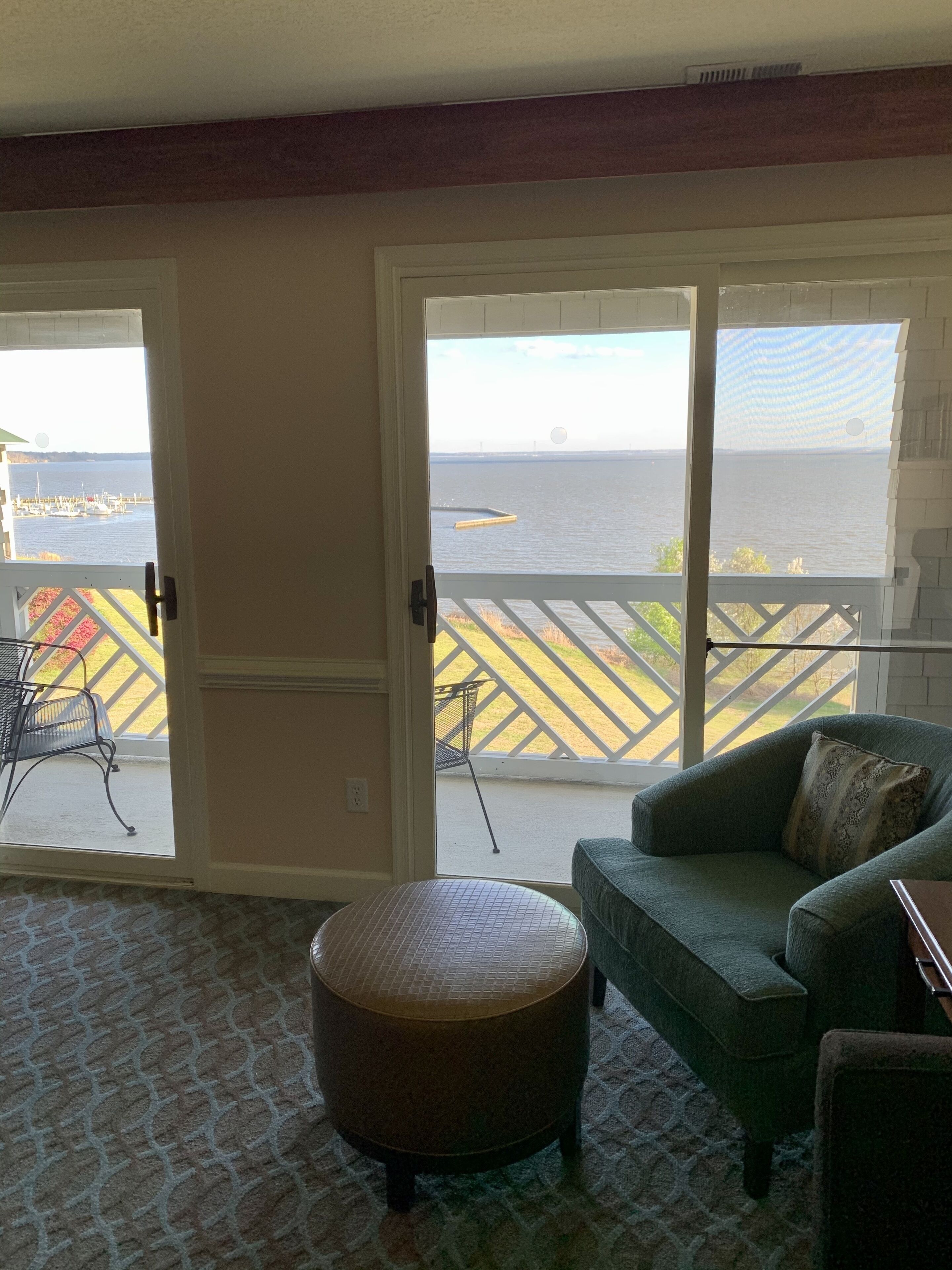 A room with a green sofa, a wicker ottoman, and a view of a marina through large sliding glass doors.