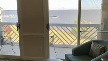 A room with a green sofa, a wicker ottoman, and a view of a marina through large sliding glass doors.