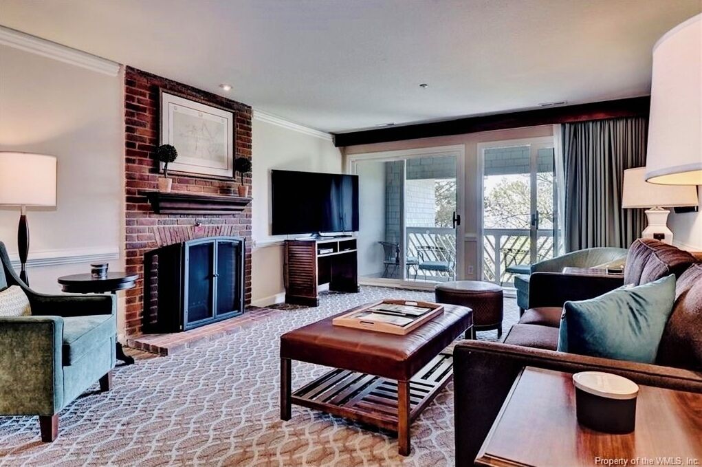 A living room with a brick fireplace, a flat-screen TV, and a large window with curtains.