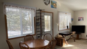 A dining area with a wooden table and chairs, a TV, and a shelving unit with various items. - Guest House at Parkland Beach, Gull Lake (Ponoka County)