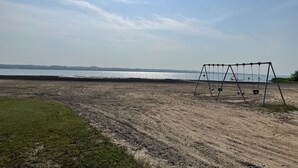 A beach with a swing set and a clear view of the water. - Guest House at Parkland Beach, Gull Lake (Ponoka County)