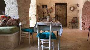 A rustic stone room with a table set for dining, a chair with a green cushion, and a wooden door. - Private boho trullo near Alberobello /Locortotondo (Martina Franca)