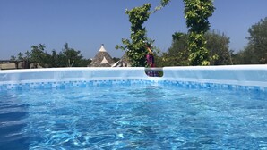 A clear blue swimming pool with a tiled edge, surrounded by trees and a thatched-roof structure. - Private boho trullo near Alberobello /Locortotondo (Martina Franca)