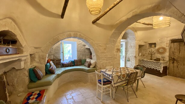 A rustic stone interior with a stone bench, a table with chairs, and a hanging light fixture. - Private boho trullo near Alberobello /Locortotondo (Martina Franca)