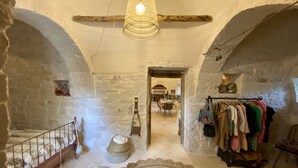 A rustic interior with exposed stone walls, a spiral staircase, and a clothing rack. - Private boho trullo near Alberobello /Locortotondo (Martina Franca)