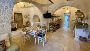 A rustic stone interior with a dining area, kitchen, and a television mounted on the wall. - Private boho trullo near Alberobello /Locortotondo (Martina Franca)