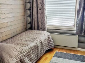 A bedroom with a bed, a radiator, a window with blinds, and a wooden floor.