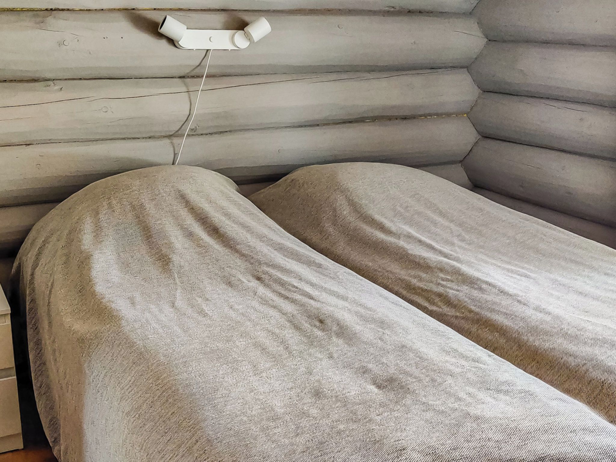 Een enkel bed met een wit hoofdbord en een witte nachtkastje met een lamp.