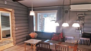 A cozy log cabin interior with a dining area, a sofa, and a window with blinds.