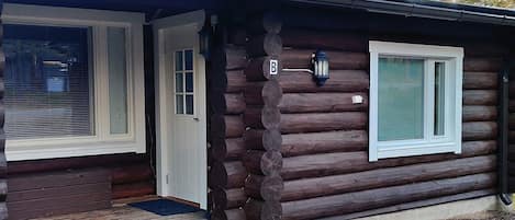 Een vakantiehuisje van hout met een voordeur, een raam en een veranda.