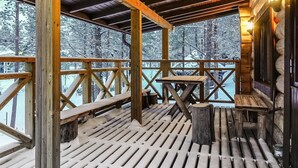 A wooden deck with benches and a table, surrounded by snow-covered trees.