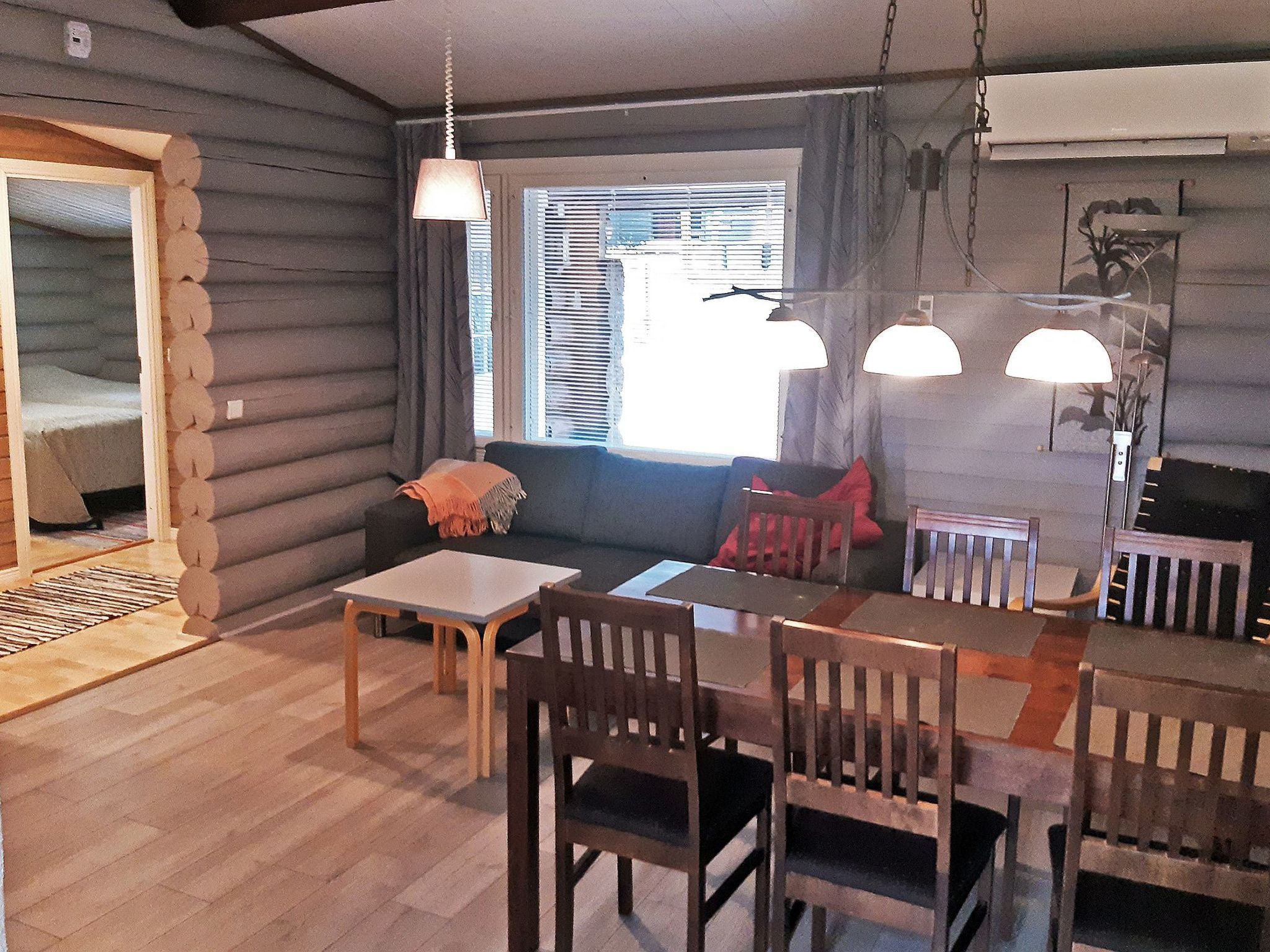L’intérieur d’une cabane en rondins comprend un coin repas, un canapé et une fenêtre avec des stores.