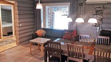 L’intérieur d’une cabane en rondins comprend un coin repas, un canapé et une fenêtre avec des stores.