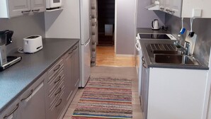 A compact kitchen with a microwave, toaster, and sink. A striped rug is on the floor, and a red fire extinguisher is mounted on the wall.