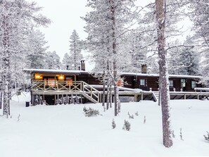 En stuga med en träveranda och en trappa som leder upp till entrén, omgiven av snötäckta träd.